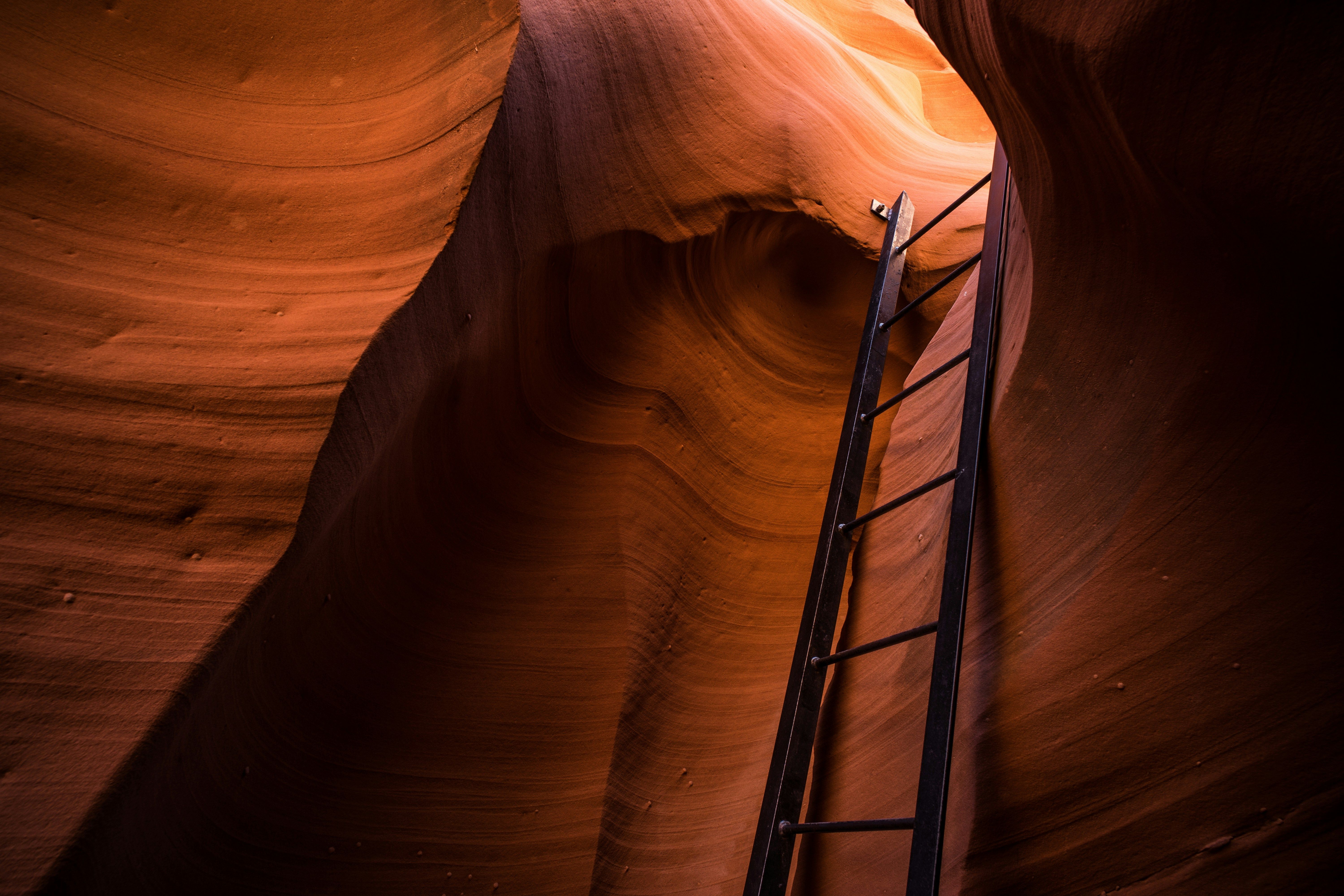 A slot canyon interior with curved orange sandstone walls and a black metal ladder for access.